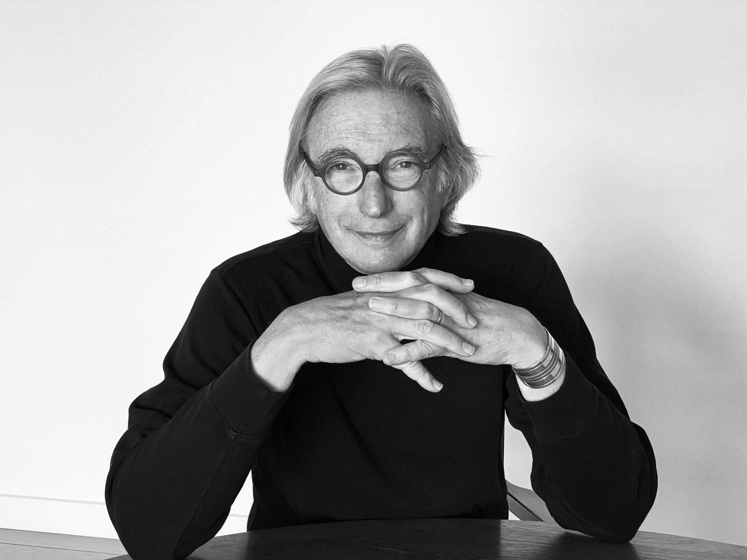 Med sine runde briller på samler  smilendeMichael Tilson Thomas fingrene under hagen med albuerne hvilende på bordet foran.
