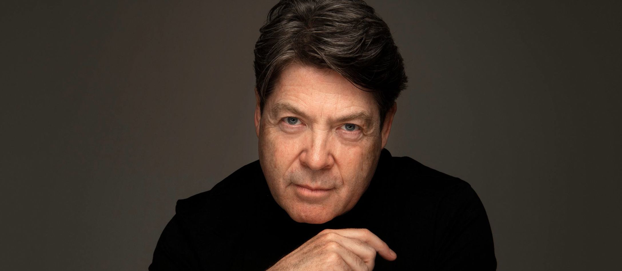 Nick Davies med mørkebrun baggrund og med dirigentpind i hånden