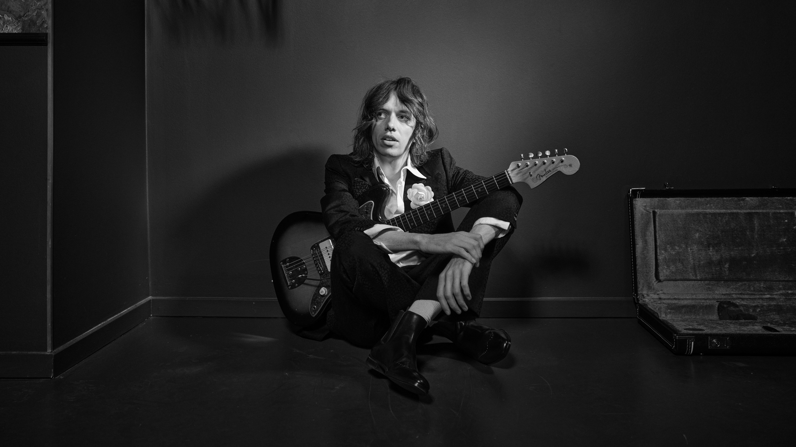 Carl Emil Petersen i sort hvid med korslagte ben og guitar i forbindelse med hans koncert i DR Koncerthus. 