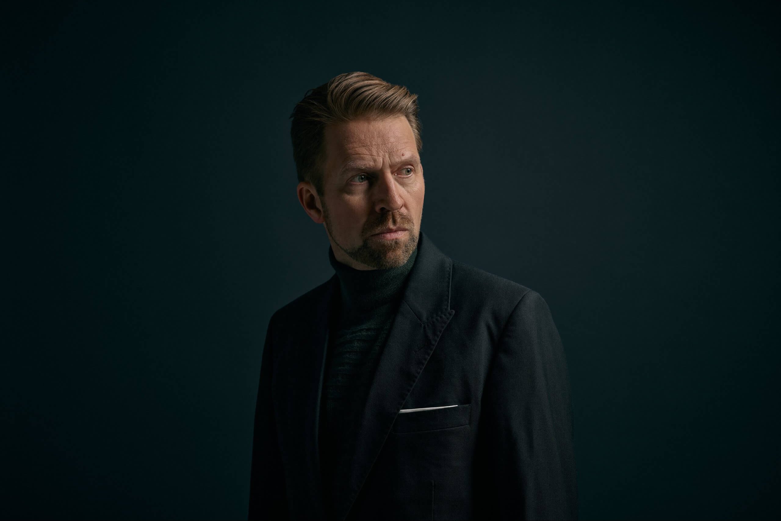 Alvorlige Leif Ove Andsnes iført helt sort jakkesæt kigger mod sin venstre på sort baggrund.