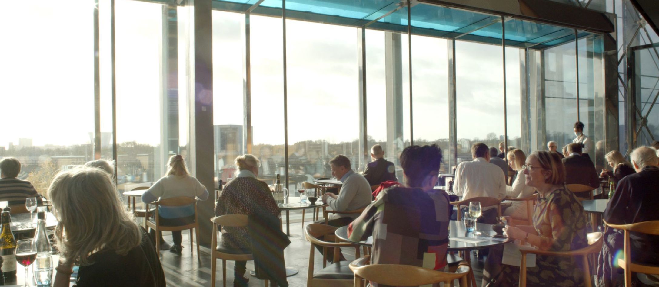 Mennesker i restauranten i DR Koncerthuset med fyldte glas kigger ud gennem viduesruderne.