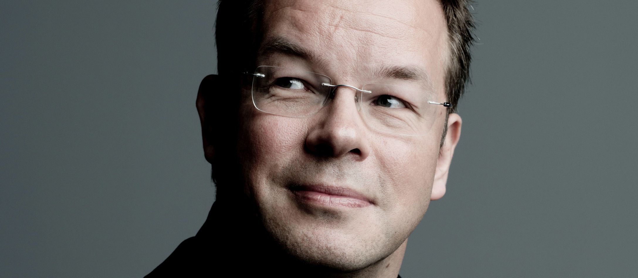 Antony Hermus iført sort skjorte foran grålig baggrund