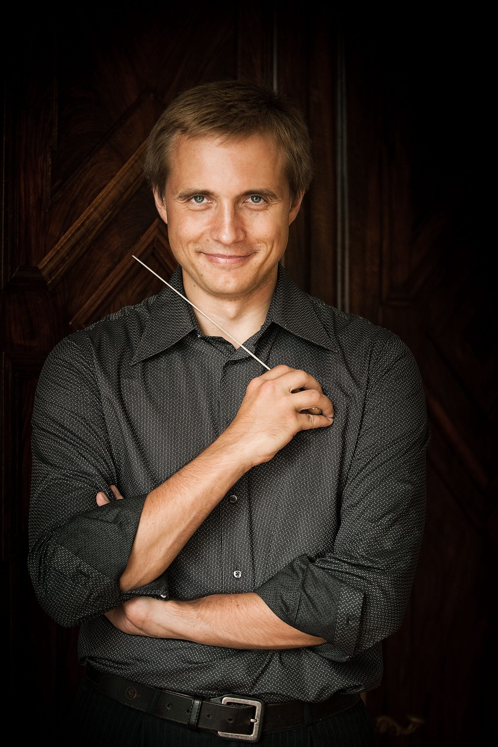 Dirigenten Vasily Petrenko med korslagte arme smiler behageligt med dirigentstang i højre hånd ført op mod ansigtet.