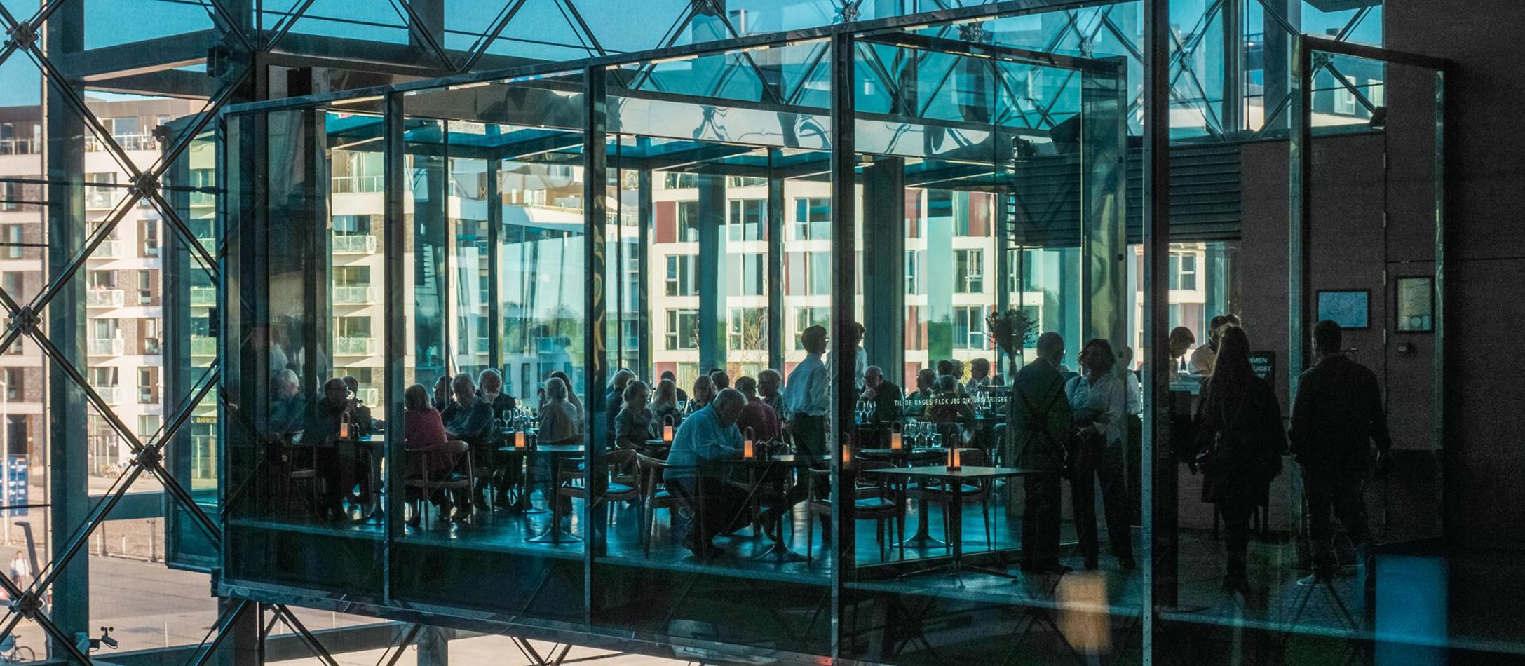 Restauranten i DR Koncerthuset set udefra igennem blå glasruder og ind til bords.