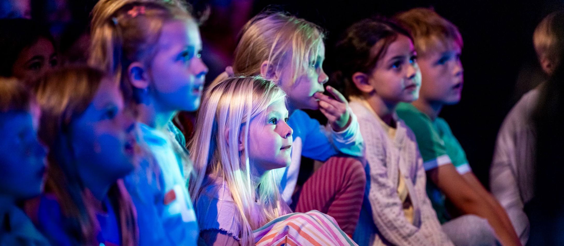 Børn til skolekoncert sidder i blåt skær og kigger på scenen