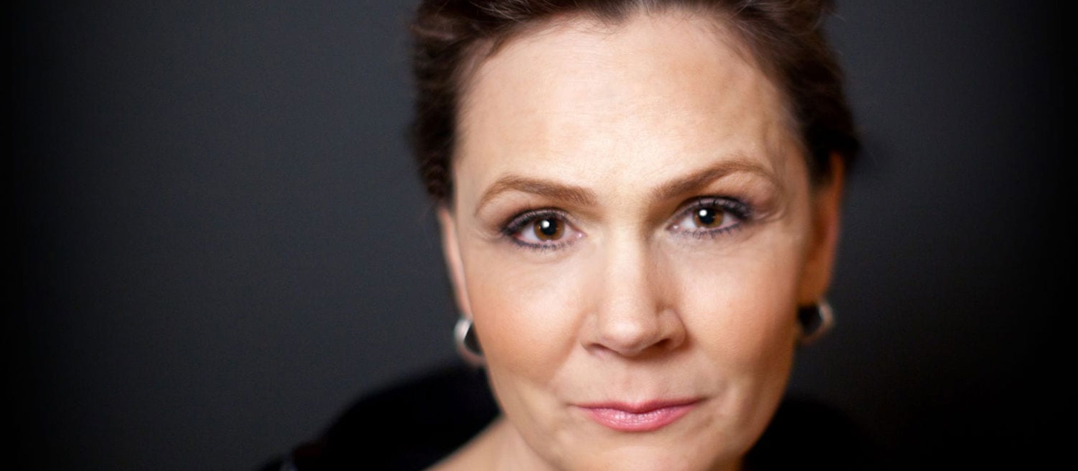 Anna Larssons smukke ansigt, håret flot opsat og dybe brune øjne foran mørkegrå baggrund
