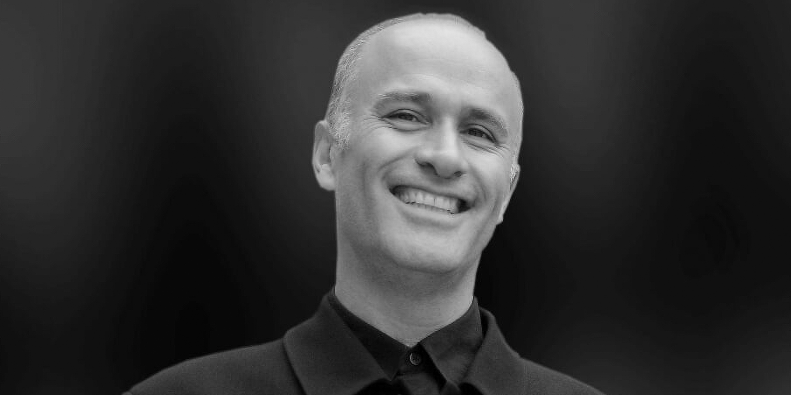 Nicholas Kok i sort/hvid står oprejst i sort klassisk, stilet efterårsjakke og smiler blidt med blottede hvide tænder.