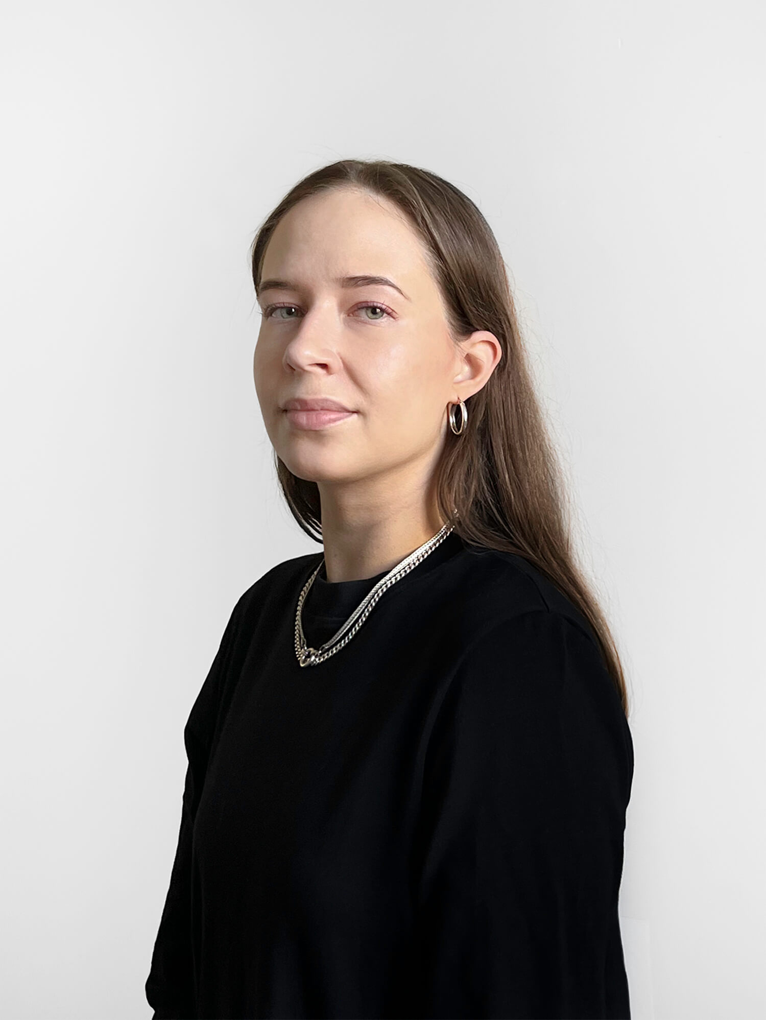Irene Suosalo med glat brunt hår og lys fin hud iført sort langarmet bluse og halvlang sølvhalskæde og runde små øreringe