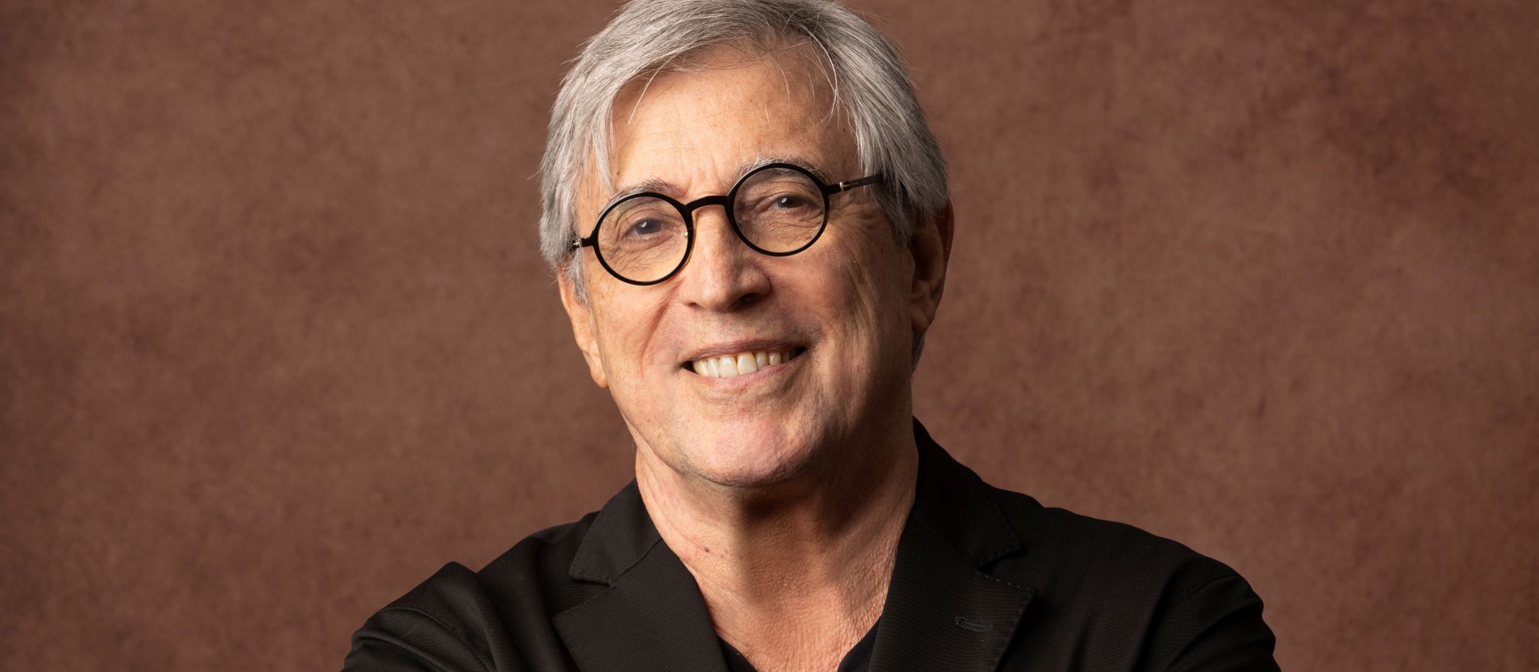 Mand i sort med briller, kigger ind i kameraet foran en brun baggrund.