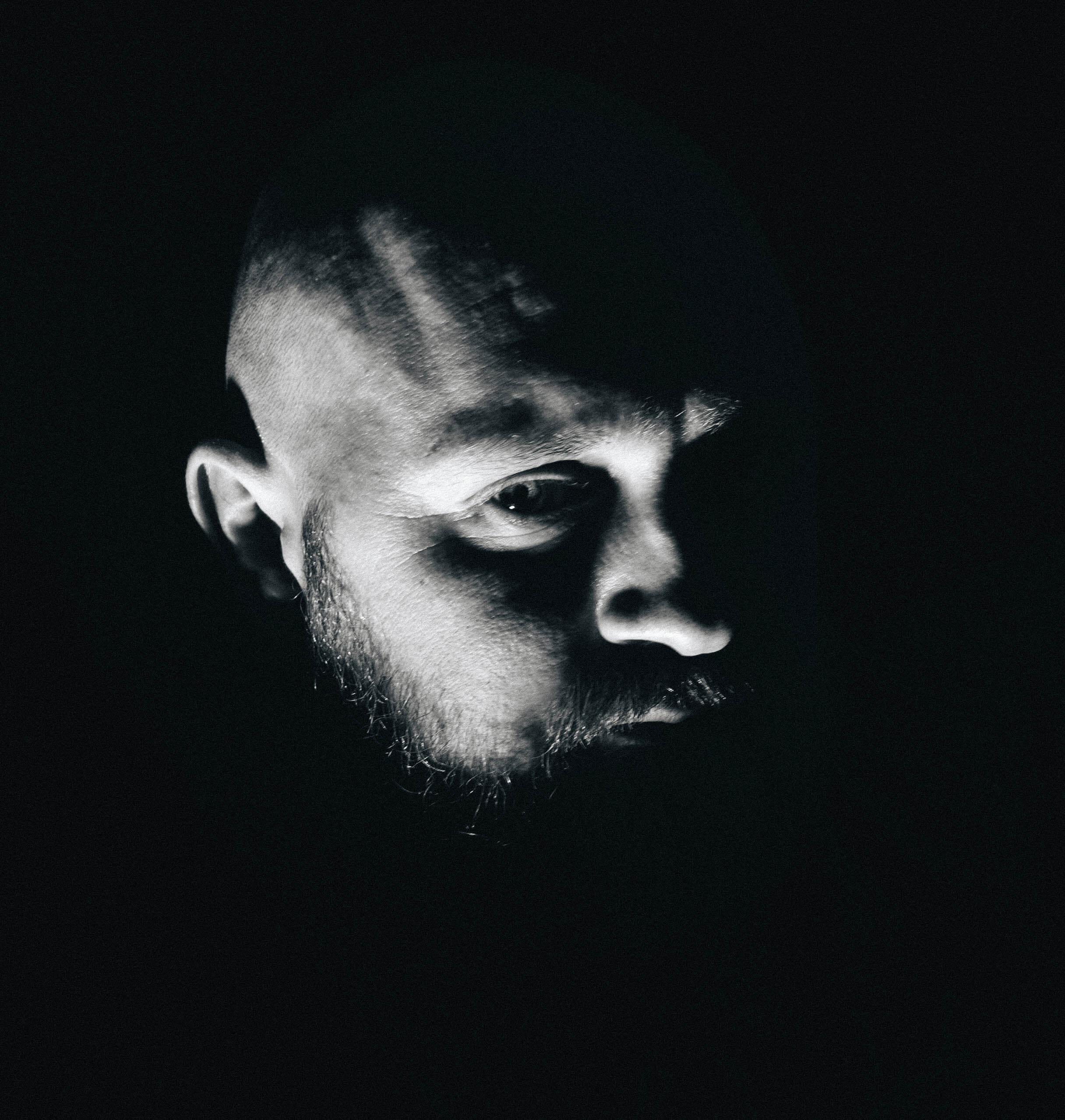 Simon Sonne Andersen i sort hvid format kun halvdelen af ansigtet oplyst meget mørkt. 