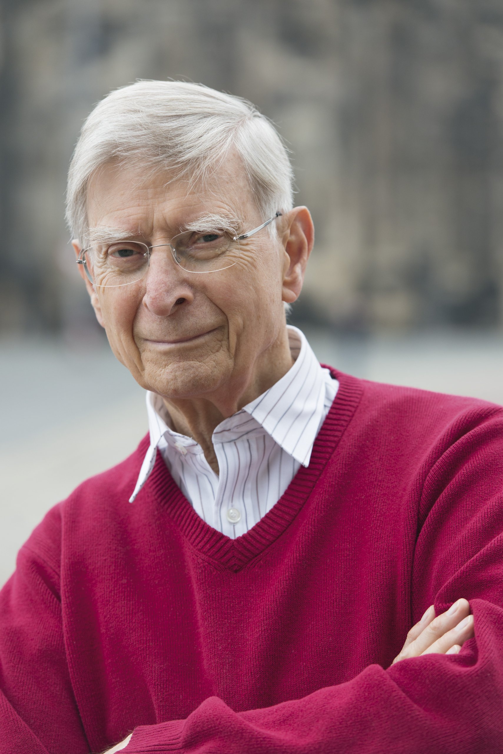 Herbert Blomstedt iført rød pullover med en hvidstribet skjorte med kortslagte arme foran sløret lys baggrund 