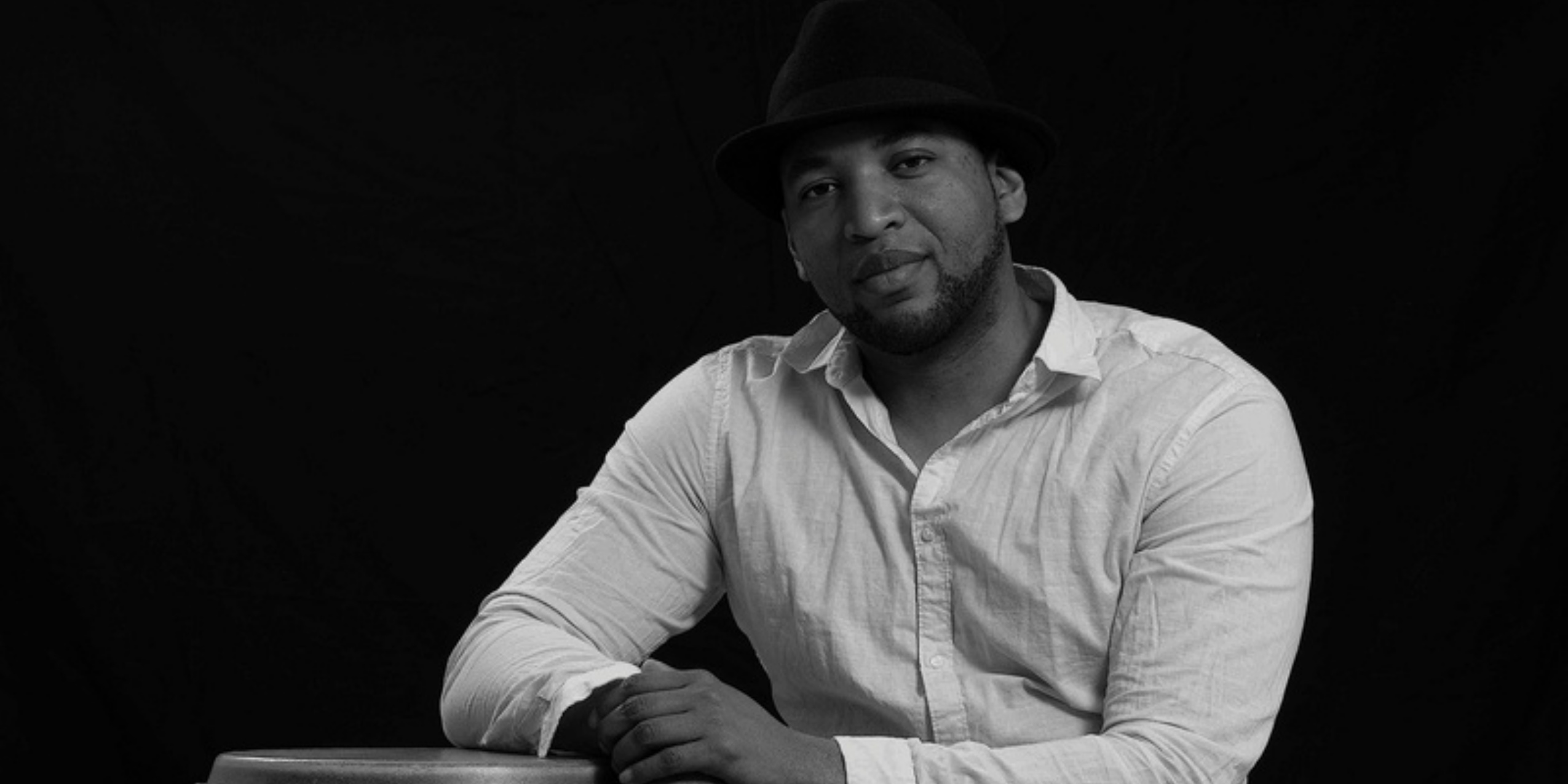 Mand i hvid skjorte og sort hat kigger ind i kameraet.