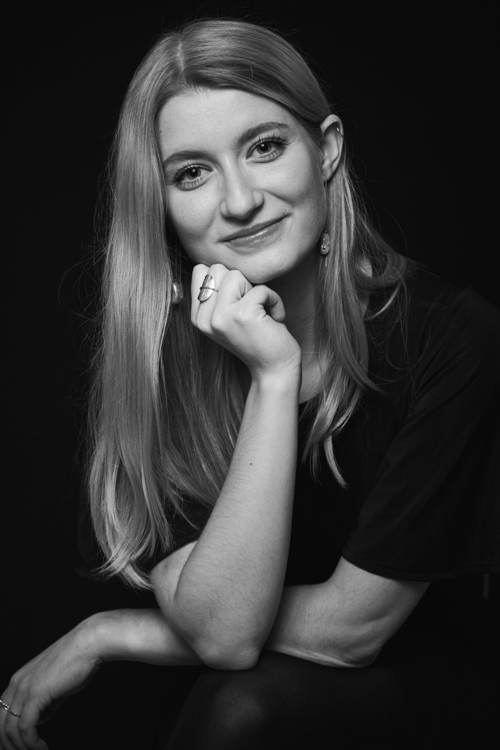 Lyshårede Louise McClelland Jacobsen i sort hvid med ansigtet hvilende på højre hånd kigger med milde øjne.
