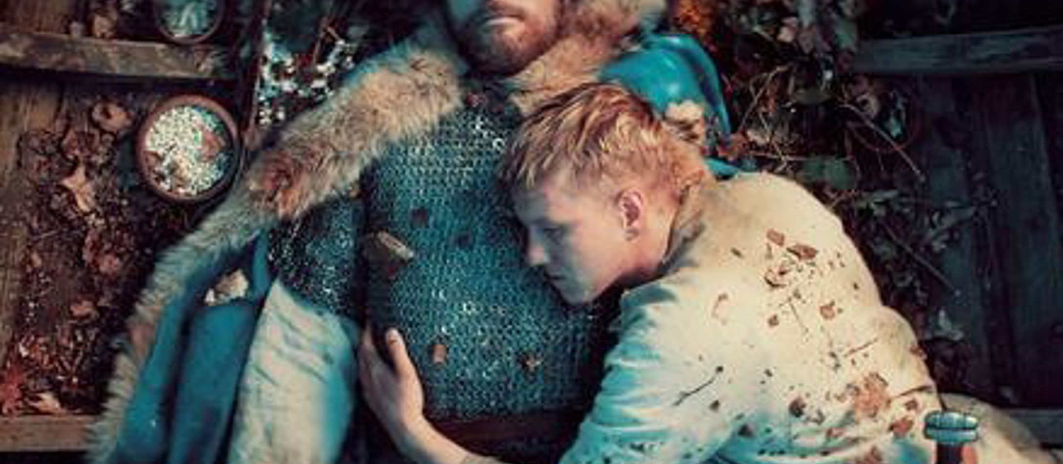 Afdød vikingekonge i bunden af båd bliver krammet af sørgende ung viking.