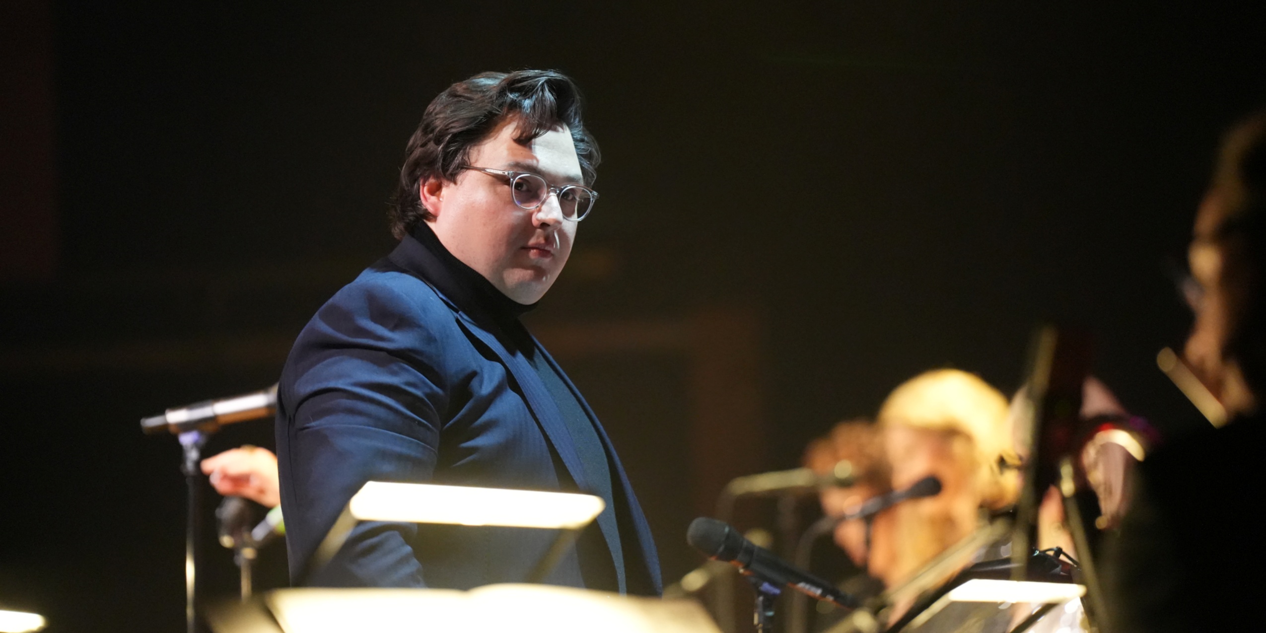 Mand står foran orkester og dirigerer.